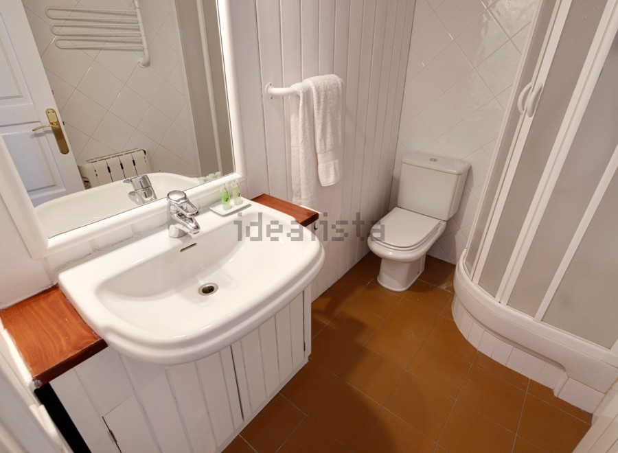 This charming bathroom boasts a modern sink and toilet, complemented by a clean white color scheme and wood accents.