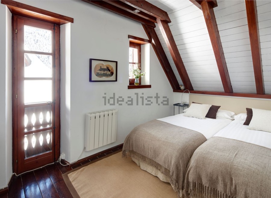Charming attic bedroom with twin beds, exposed wooden beams, and a rustic wooden door leading to outdoor views.