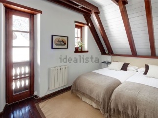 Charming attic bedroom with twin beds, exposed wooden beams, and a rustic wooden door leading to outdoor views.