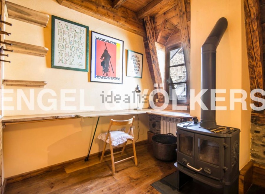 Charming attic room with wooden beams, featuring a built-in desk and a wood-burning stove.