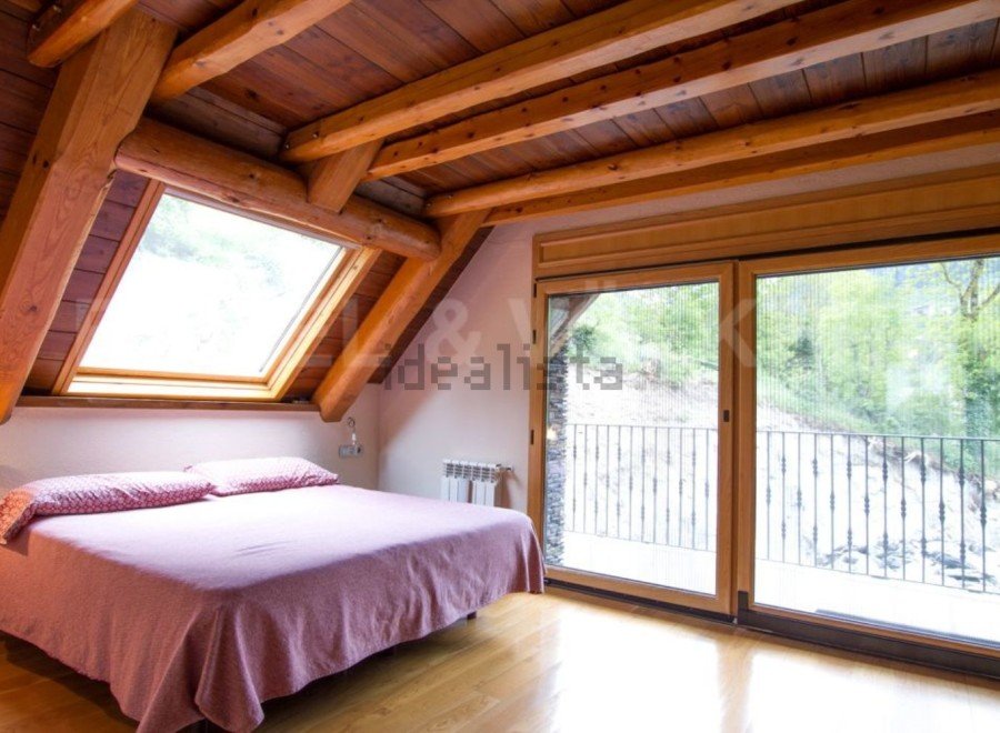 Cozy attic bedroom with wooden beams and large windows offering stunning views.