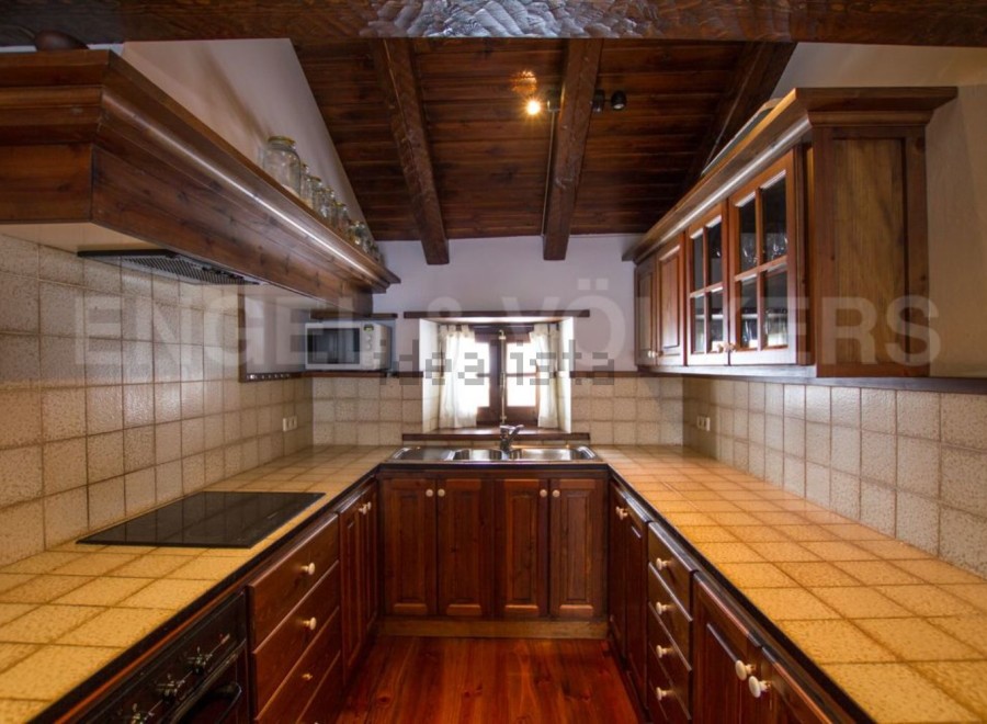 Rustic kitchen with wooden beams and tiled countertops.