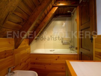 Charming attic bathroom with wooden walls and beams, featuring a bathtub and shower.