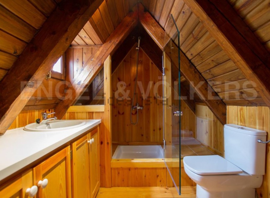Charming attic bathroom with wood paneling, a shower stall, and a toilet.
