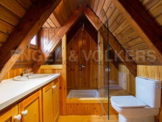Charming attic bathroom with wood paneling, a shower stall, and a toilet.