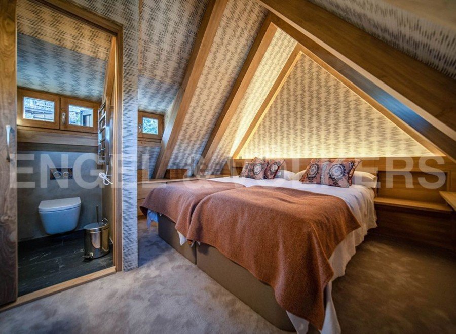 This stunning attic bedroom boasts a unique sloped ceiling with exposed wooden beams and stylish wallpaper.