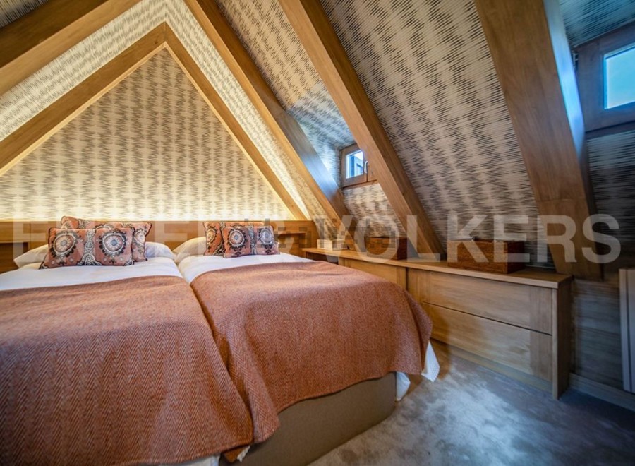 Cosy attic bedroom with twin beds, featuring a unique sloped ceiling and wooden beams.