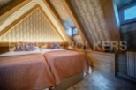 Cosy attic bedroom with twin beds, featuring a unique sloped ceiling and wooden beams.