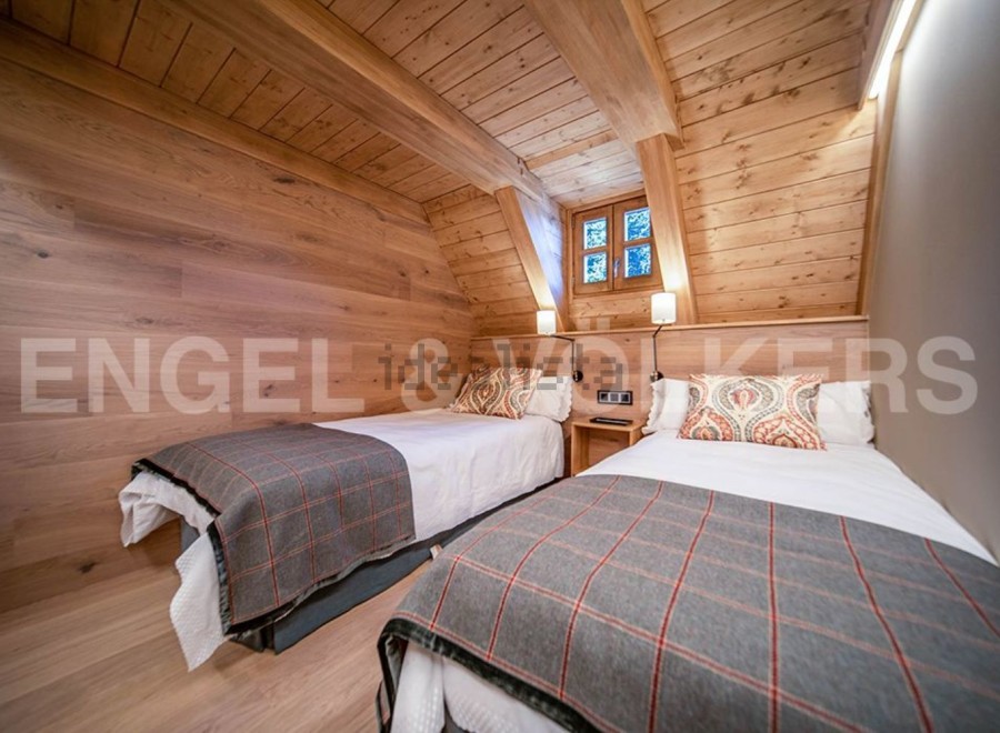 Cozy chalet bedroom with twin beds, wooden walls and ceiling, and a window offering views of nature.