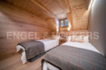 Cozy chalet bedroom with twin beds, wooden walls and ceiling, and a window offering views of nature.
