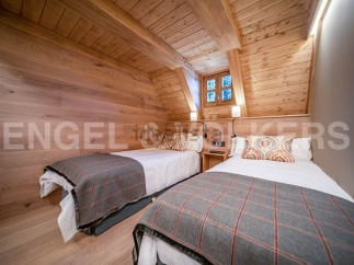 Cozy chalet bedroom with twin beds, wooden walls and ceiling, and a window offering views of nature.