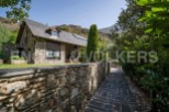Mountainside stone house with slate roof, large windows, and a stone wall pathway.
