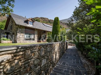 Mountainside stone house with slate roof, large windows, and a stone wall pathway.