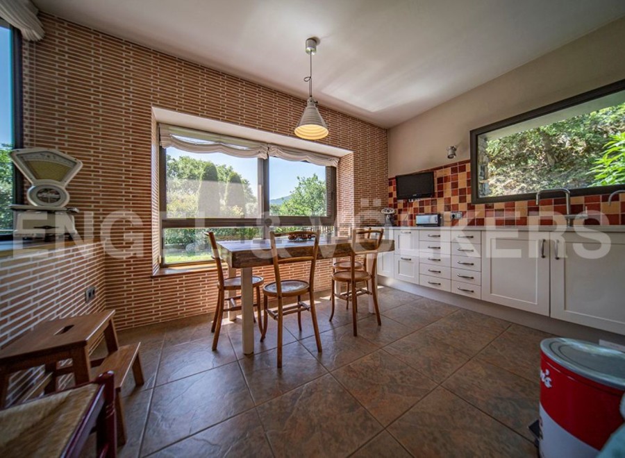 Rustic kitchen with brick feature wall, large windows overlooking garden, and white shaker-style cabinets.