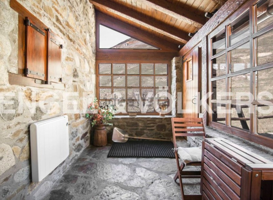 Rustic stone cottage with wooden beams and large windows offering stunning mountain views.