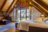 This stunning attic bedroom boasts a cozy wooden interior, large windows offering breathtaking mountain views, and a comfortable bed with plush bedding.