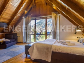 This stunning attic bedroom boasts a cozy wooden interior, large windows offering breathtaking mountain views, and a comfortable bed with plush bedding.