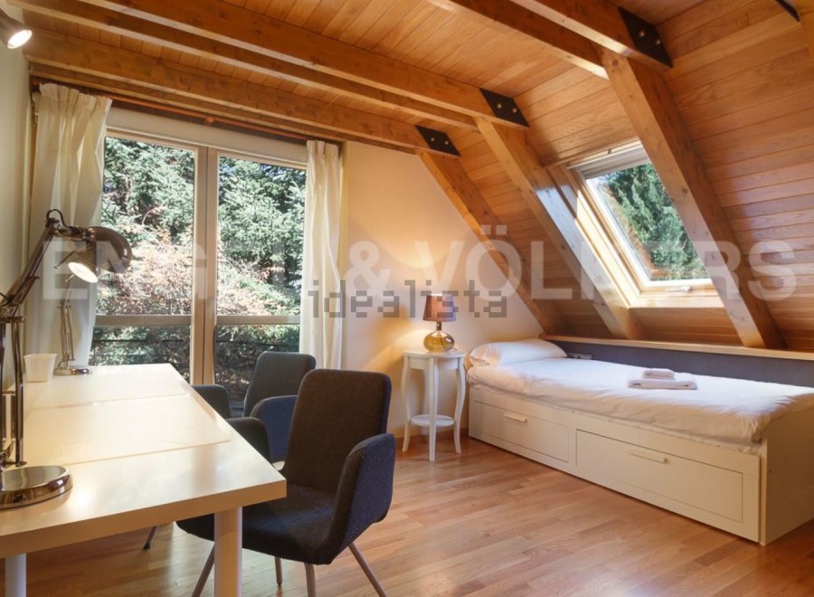 Charming attic room with wooden beams, large windows offering scenic views, and a built-in bed with storage.