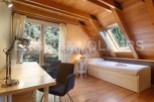 Charming attic room with wooden beams, large windows offering scenic views, and a built-in bed with storage.