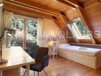Charming attic room with wooden beams, large windows offering scenic views, and a built-in bed with storage.