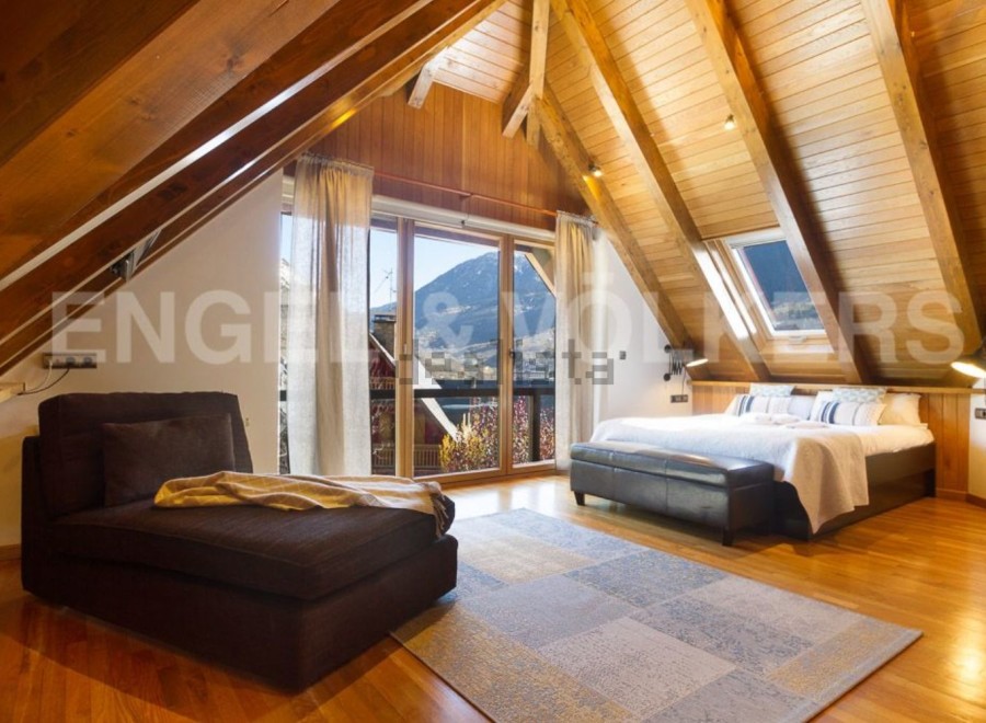 This stunning attic bedroom boasts a wood-beamed ceiling, large windows offering mountain views, and a luxurious feel.