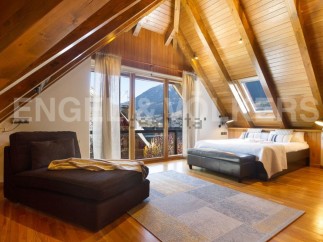 This stunning attic bedroom boasts a wood-beamed ceiling, large windows offering mountain views, and a luxurious feel.