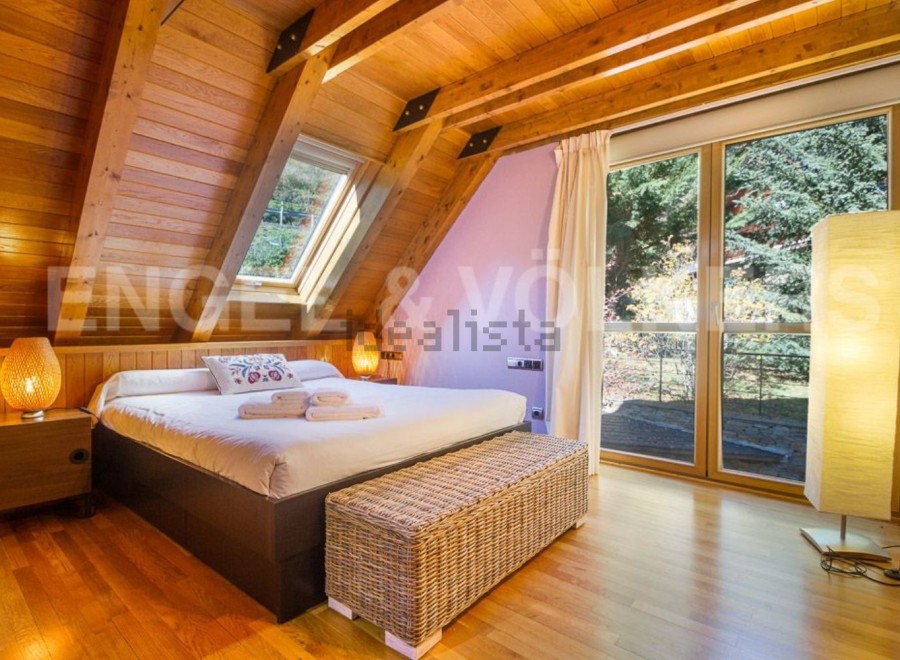 Cozy chalet bedroom with wooden beams, large windows offering scenic views, and a comfortable bed.