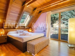 Cozy chalet bedroom with wooden beams, large windows offering scenic views, and a comfortable bed.