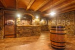 This stunning wine cellar boasts a rustic-chic design with exposed stone walls, a wooden beamed ceiling, and terracotta tile flooring.