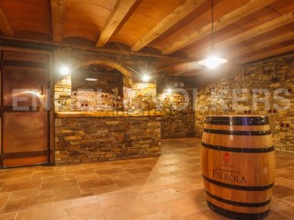 This stunning wine cellar boasts a rustic-chic design with exposed stone walls, a wooden beamed ceiling, and terracotta tile flooring.