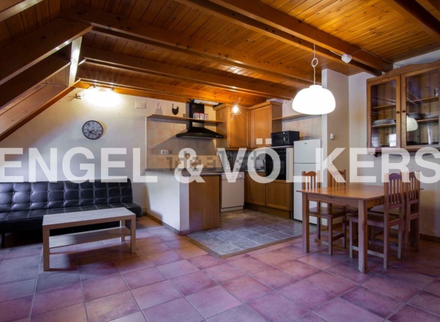 Cozy attic apartment with exposed wooden beams, open-plan kitchen and living area, and a small dining space.