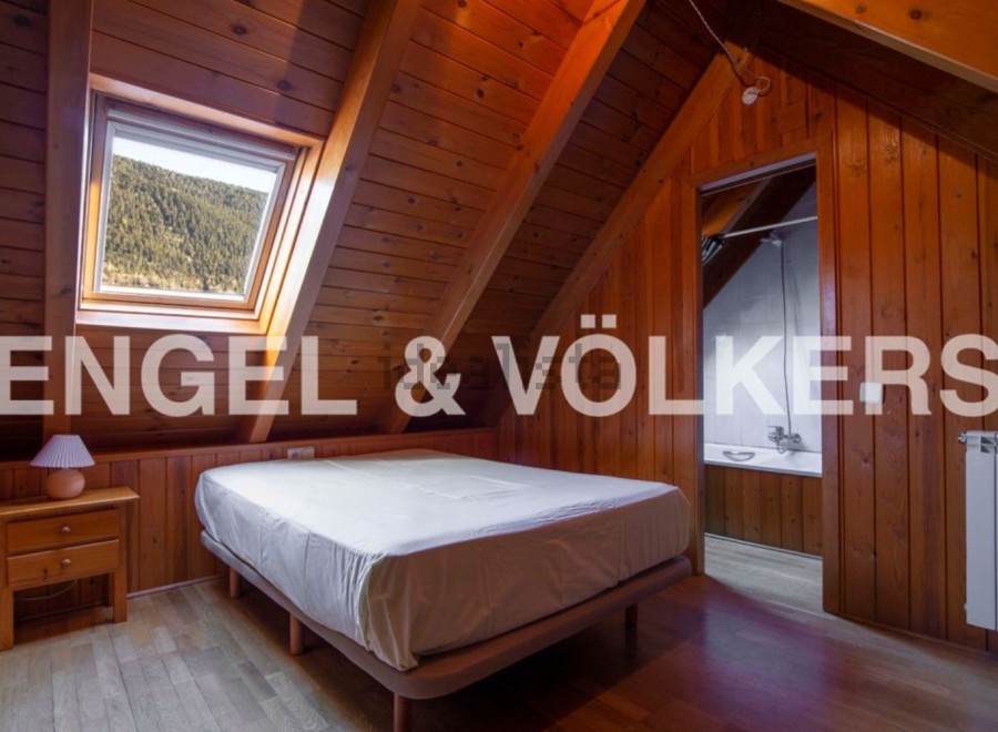 Cozy attic bedroom with wooden walls and a skylight offering stunning mountain views.