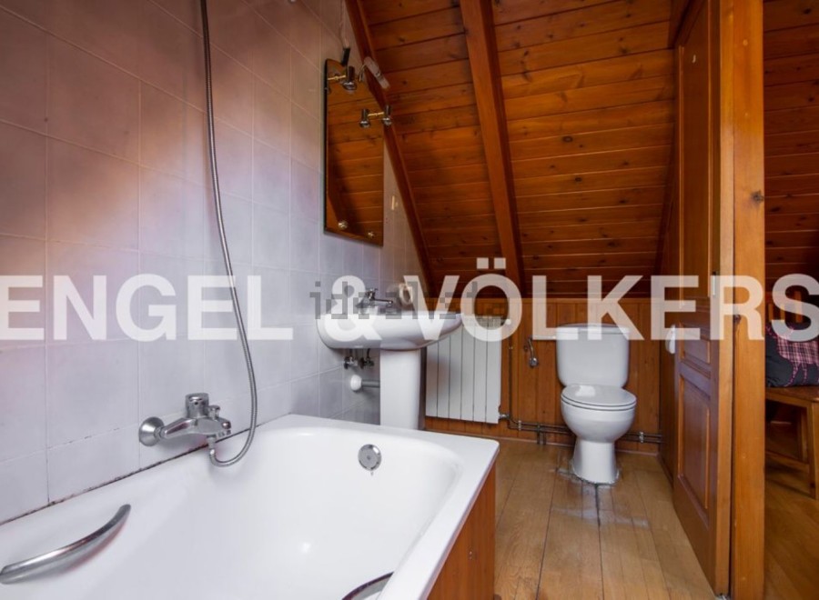 Charming attic bathroom with wooden beams, bathtub, toilet, and pedestal sink.