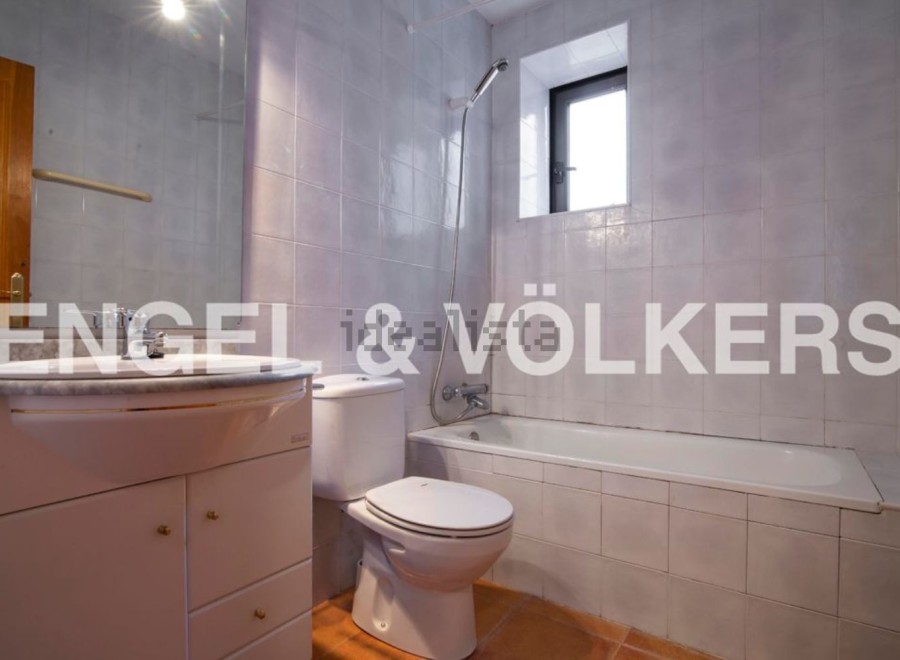 This charming bathroom boasts a classic white suite, including a bathtub and toilet, complemented by a sleek vanity unit with marble top.