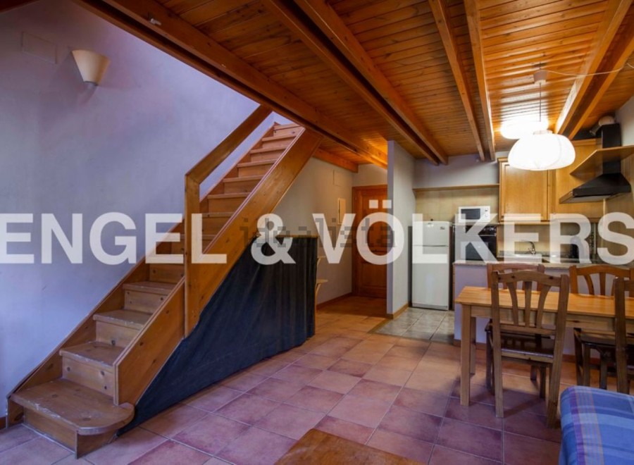Cozy apartment featuring a wooden staircase, open kitchen with dining area, and terracotta tile floors.