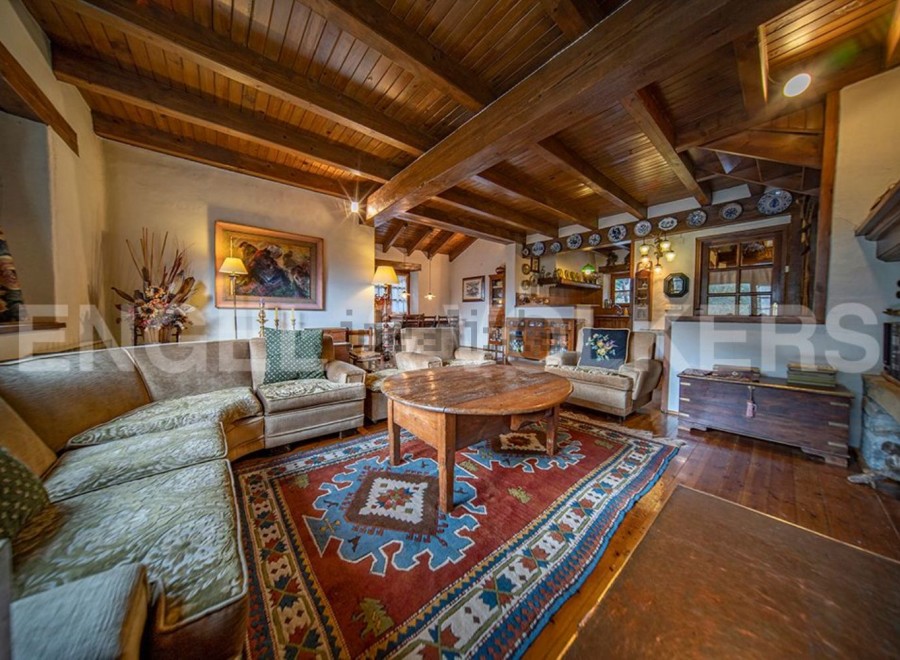 Rustic mountain chalet with exposed wooden beams and a cozy living area featuring a large, ornate rug and comfortable seating.