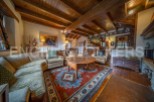 Rustic mountain chalet with exposed wooden beams and a cozy living area featuring a large, ornate rug and comfortable seating.