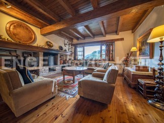 Rustic living room with wooden beams, stone fireplace, and large windows offering scenic views.