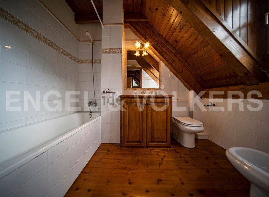 Charming attic bathroom with wooden beams, a bathtub, and a toilet.