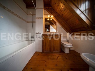 Charming attic bathroom with wooden beams, a bathtub, and a toilet.