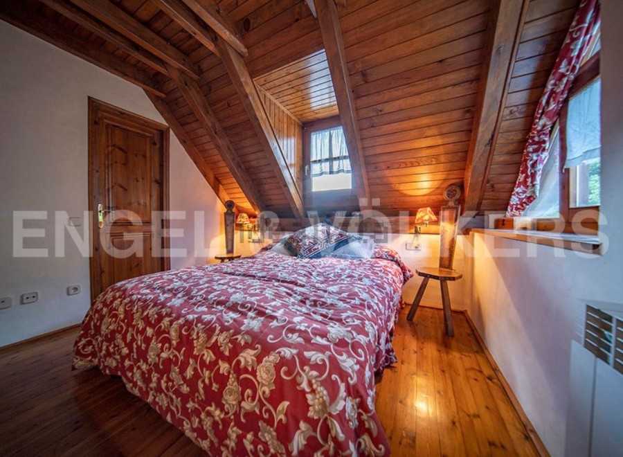 Cozy attic bedroom with wooden beams, floral bedding, and warm lighting.