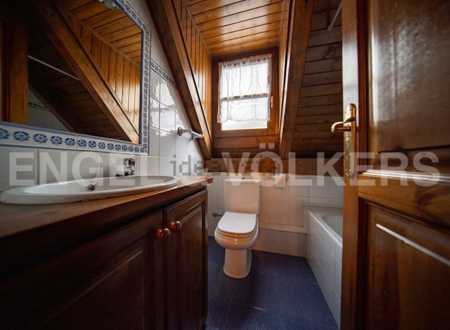 Charming attic bathroom with wooden beams, white tiled walls, and a wooden vanity.