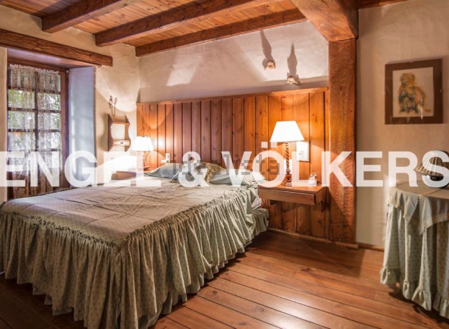 Rustic bedroom with wooden beams and floors, featuring a comfortable bed with a ruffled bedskirt and wooden headboard.