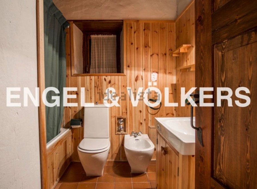 Rustic bathroom with wooden walls and floors, featuring a toilet, bidet, bathtub, and sink.