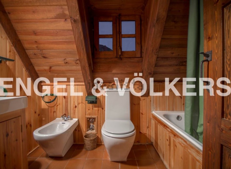 Rustic bathroom with wooden walls and ceiling, featuring a toilet, bidet, bathtub, and a small window offering mountain views.