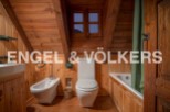 Rustic bathroom with wooden walls and ceiling, featuring a toilet, bidet, bathtub, and a small window offering mountain views.