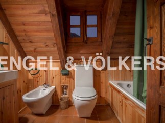Rustic bathroom with wooden walls and ceiling, featuring a toilet, bidet, bathtub, and a small window offering mountain views.