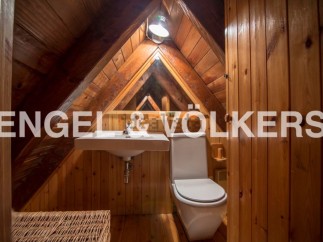 Charming attic bathroom with wooden walls and beams, featuring a sink, toilet, and wicker storage.