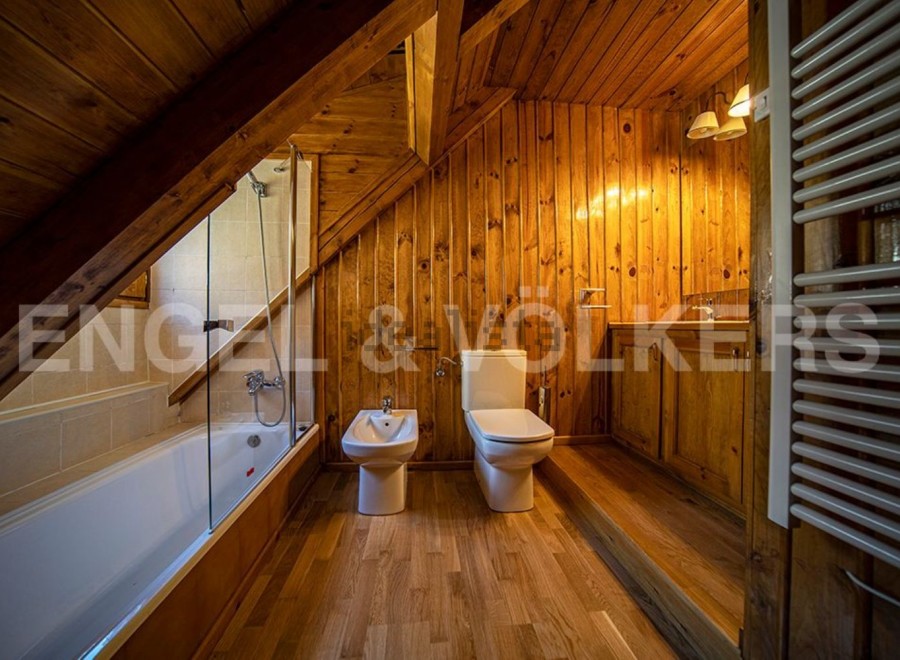 Charming attic bathroom with wooden walls and floors, featuring a bathtub, toilet, and bidet.