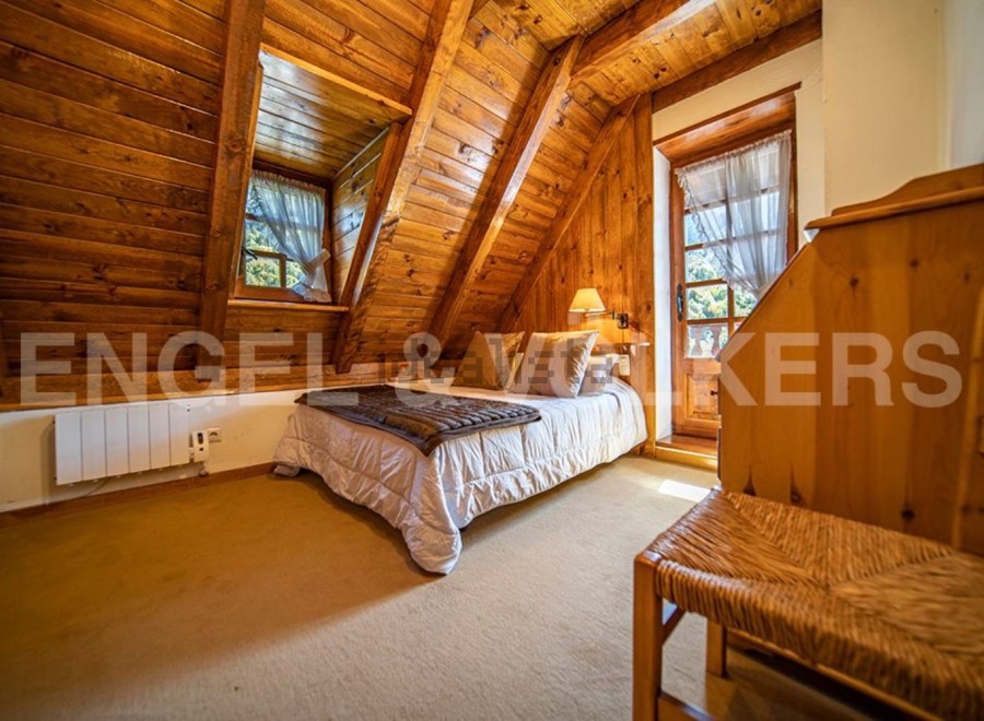Cozy chalet bedroom with wooden walls and ceilings, featuring a comfortable double bed and a charming wicker chair.